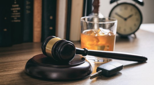An alcoholic beverage and set of car keys sit on a desk next to a judge's mallet. 